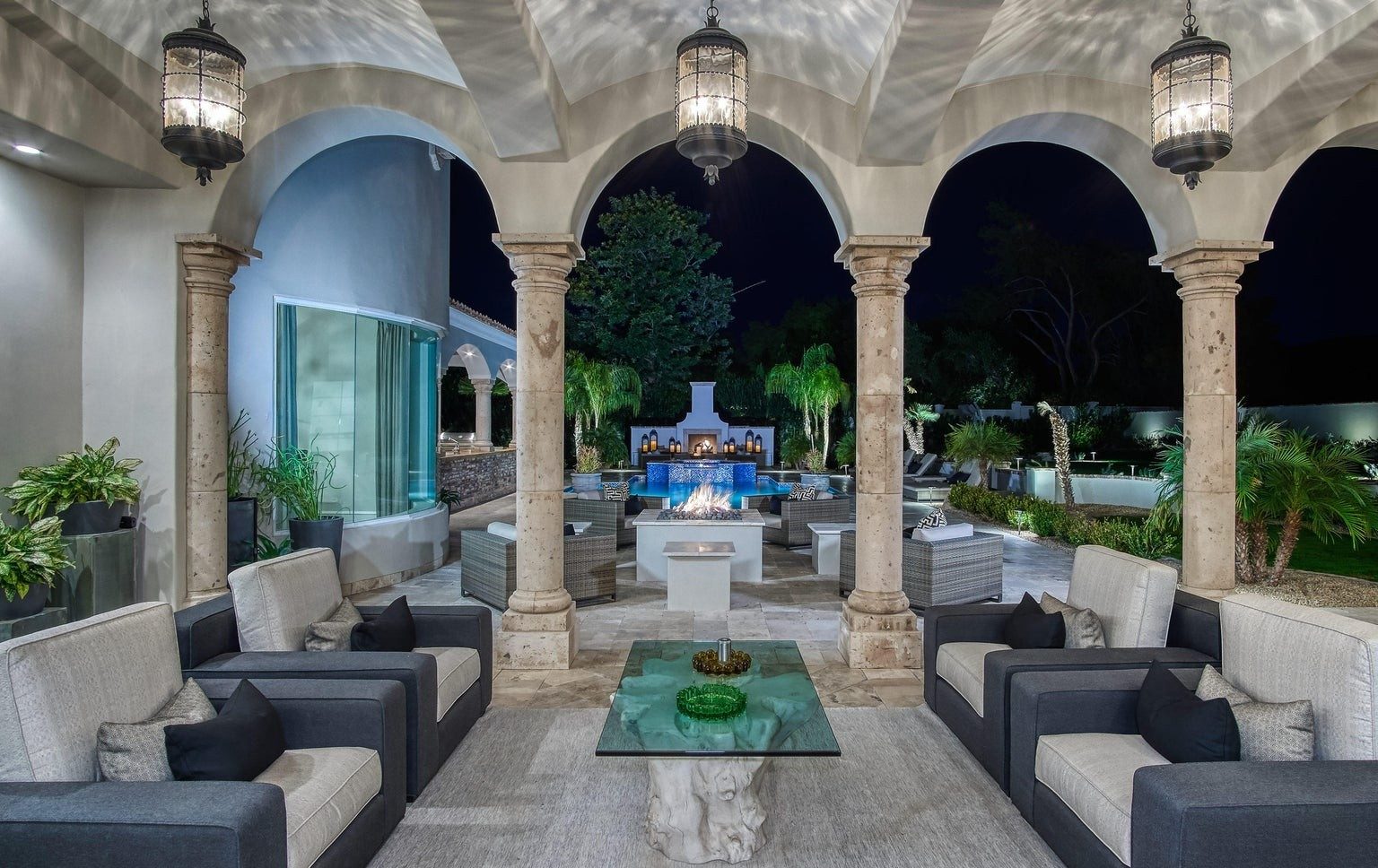 Arched stone loggia and fire feature overlooking a lit pool at night